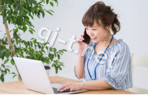 パソコンしながら電話をするストライプの服の女性